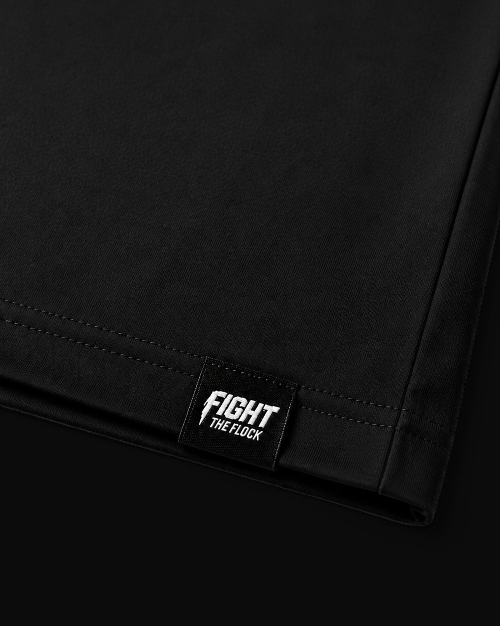 Close-up of a black fabric product corner with a small black brand patch reading “FIGHT THE FLOCK” in white text.